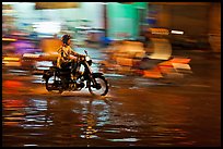 Motorcyclist speeding on wet street at night, with streaks giving sense of motion. Ho Chi Minh City, Vietnam