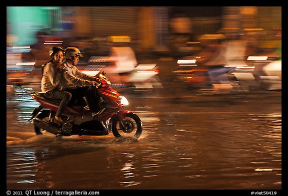 Couple sharing fast night ride on wet street. Ho Chi Minh City, Vietnam (color)