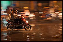 Couple sharing fast night ride on wet street. Ho Chi Minh City, Vietnam