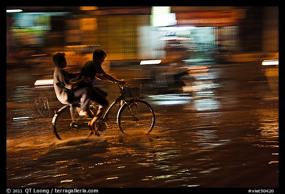 Men sharing bicycle ride at night on wet street. Ho Chi Minh City, Vietnam