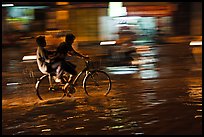 Men sharing bicycle ride at night on wet street. Ho Chi Minh City, Vietnam