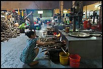 Woman feeding furnace in cococut candy factory. Ben Tre, Vietnam