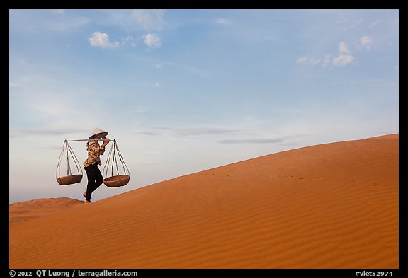 Woman with yoke baskets walks on sand dunes. Mui Ne, Vietnam