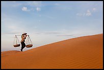 Woman with yoke baskets walks on sand dunes. Mui Ne, Vietnam ( color)