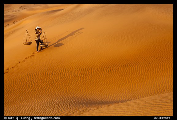 Woman walking with baskets on sands. Mui Ne, Vietnam (color)