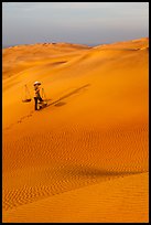 Rippled red sand dunes and woman with baskets. Mui Ne, Vietnam ( color)