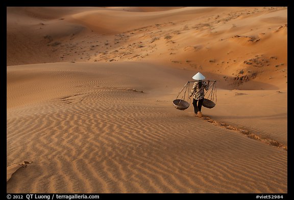 Woman with conical hat carries pannier baskets. Mui Ne, Vietnam (color)