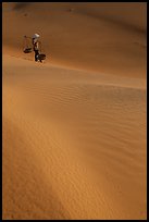 Woman with conical hat and shoulder pole baskets pauses on dune. Mui Ne, Vietnam (color)