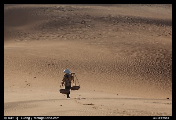 Woman walking on dune field with yoke baskets. Mui Ne, Vietnam
