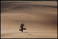 Woman walking on dune field with yoke baskets. Mui Ne, Vietnam (color)