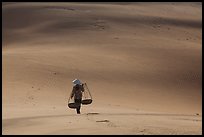 Woman walking on dune field with yoke baskets. Mui Ne, Vietnam (color)