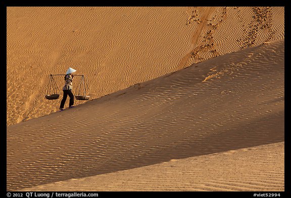 Woman ascending dune ridge with two baskets. Mui Ne, Vietnam (color)