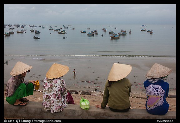 Four women in conical hats watch fishing activity from high above fishing village. Mui Ne, Vietnam (color)