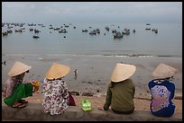 Four women in conical hats watch fishing activity from high above fishing village. Mui Ne, Vietnam (color)