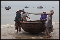 Fishermen carry round woven boat to shore. Mui Ne, Vietnam (color)