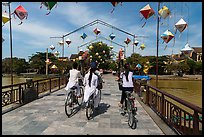 Girls on bicycle cross bridge festoned with lanterns. Hoi An, Vietnam (color)