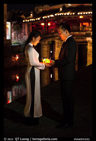 Couple holding candles in front of Japanese bridge at night. Hoi An, Vietnam (color)