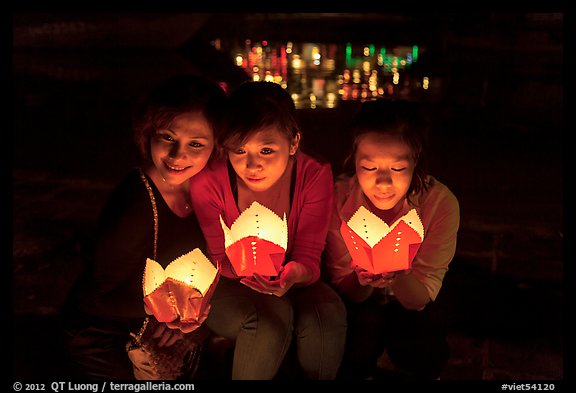 Faces of three women in the glow of candle boxes. Hoi An, Vietnam (color)