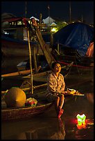 Woman sitting in boat with floating candles by night. Hoi An, Vietnam (color)