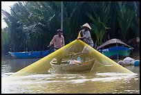Fisherman pulls up net from rowboat. Hoi An, Vietnam (color)