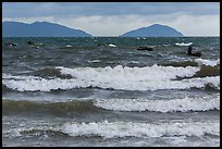 Man rowing coracle boat in distance amidst large waves. Da Nang, Vietnam (color)