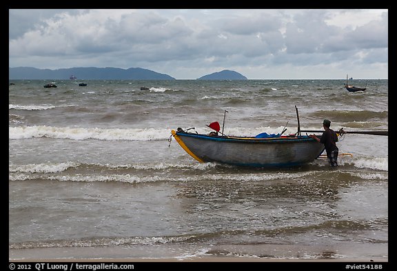 Man entering ocean with boat in stormy weather. Da Nang, Vietnam (color)
