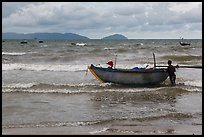 Man entering ocean with boat in stormy weather. Da Nang, Vietnam (color)