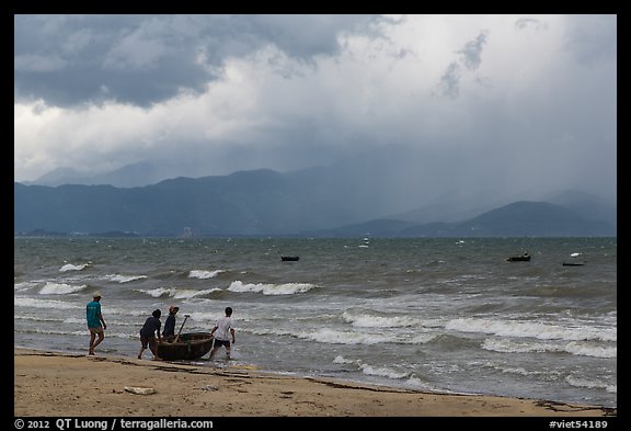 Men pushing coracle boat into stormy ocean. Da Nang, Vietnam