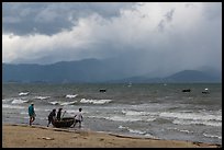 Men pushing coracle boat into stormy ocean. Da Nang, Vietnam (color)