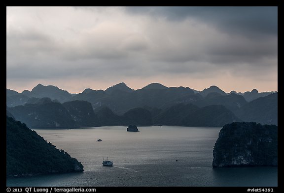 Boat amongst islands under dark sky. Halong Bay, Vietnam (color)