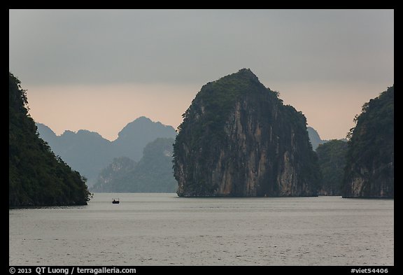 Fishing boat dwarfed by limestone islands. Halong Bay, Vietnam