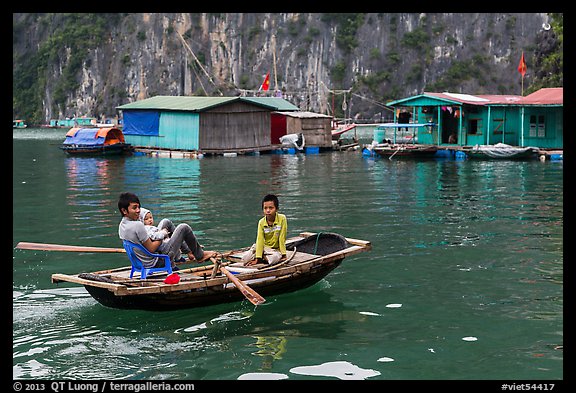 Man holding infant while rowing with feet, Vung Vieng village. Halong Bay, Vietnam