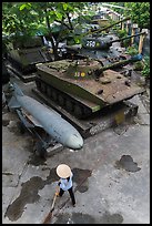 Woman sweeping floor in front of military hardware, military museum. Hanoi, Vietnam (color)