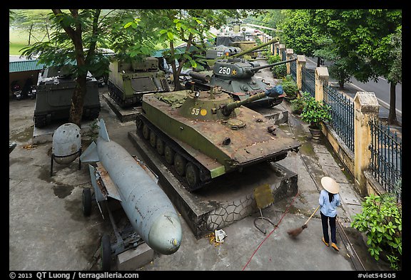 Woman sweeping floor in front of tanks, military museum. Hanoi, Vietnam