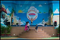 Children on stage next to militaristic mural, Dam Sen Water Park, district 11. Ho Chi Minh City, Vietnam (color)