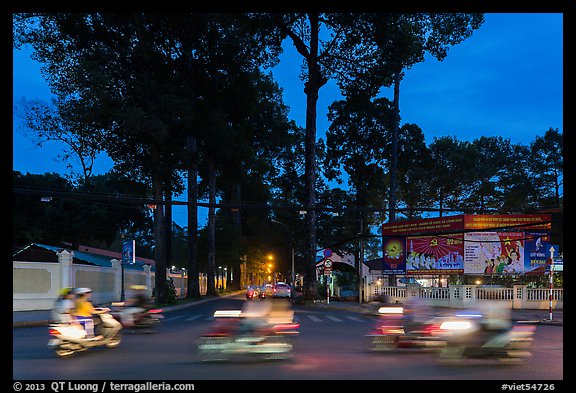 Blurred motorbikes at dusk and tall trees next to Van Hoa Park. Ho Chi Minh City, Vietnam (color)