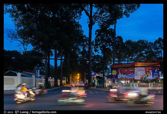 Blurred motorbikes at dusk and tall trees next to Van Hoa Park. Ho Chi Minh City, Vietnam