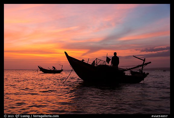 Men on fishing skiffs under bright sunset skies. Mui Ne, Vietnam (color)