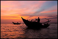 Men on fishing skiffs under bright sunset skies. Mui Ne, Vietnam (color)