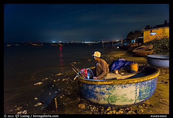 Man working on coracle boat at night. Mui Ne, Vietnam (color)