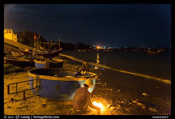 Man with fire next to coracle boat at night. Mui Ne, Vietnam (color)