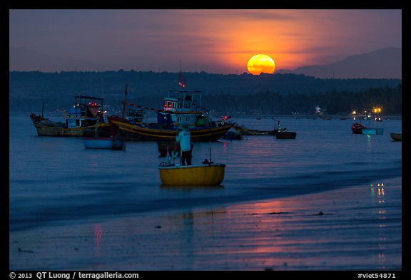 Fisherman paddling on coracle boat towards fishing boats at moonset. Mui Ne, Vietnam