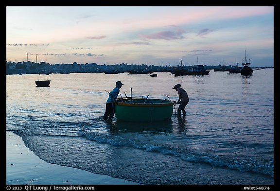 Fishermen pushing coracle boat at dawn. Mui Ne, Vietnam (color)