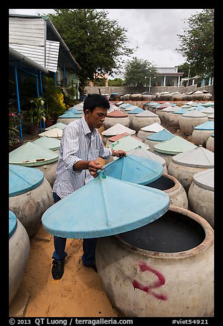Man lifting covers of jars with fermented fish sauce. Mui Ne, Vietnam (color)