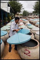 Man lifting covers of jars with fermented fish sauce. Mui Ne, Vietnam (color)