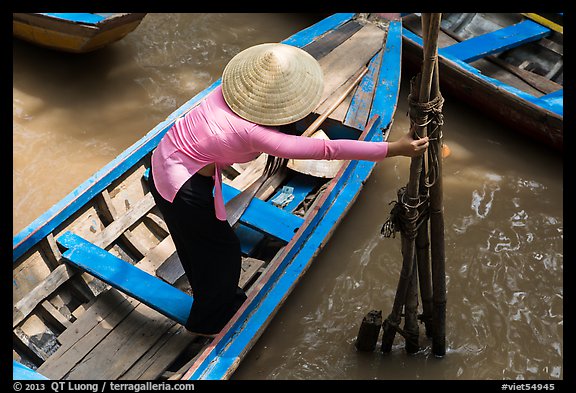 Woman in ao dai reaching to bamboo poles from boat. My Tho, Vietnam