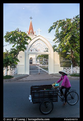 Woman bicycling in front of church. Tra Vinh, Vietnam