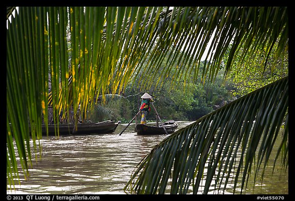 Woman paddling boat on river channel, framed by leaves. Can Tho, Vietnam (color)