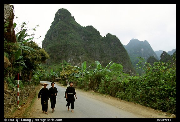 Villagers in traditional garb walking down the road with limestone peaks in the background, Ma Phuoc Pass area. Northeast Vietnam