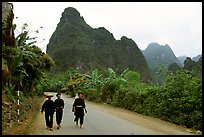 Villagers in traditional garb walking down the road with limestone peaks in the background, Ma Phuoc Pass area. Northeast Vietnam